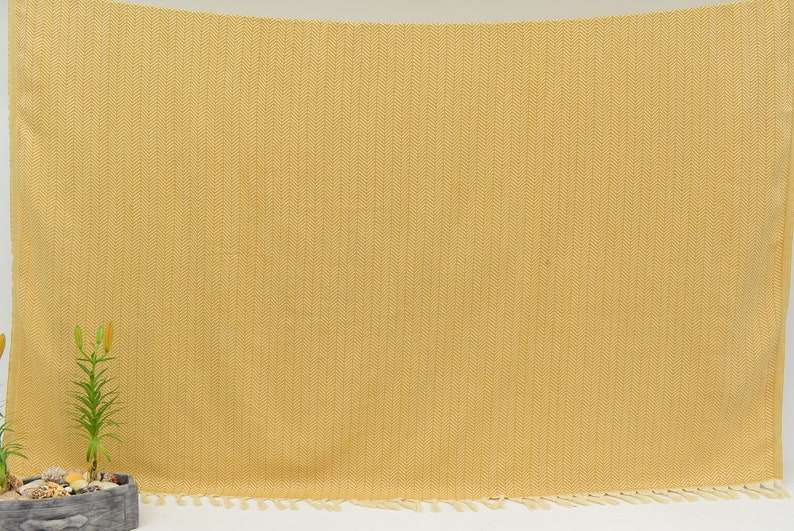 Op de afbeelding: Een gele deken met een herringbone patroon en franjes.