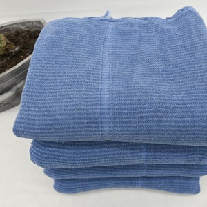 May include: A stack of four blue cotton towels. The towels are folded and have a textured weave.