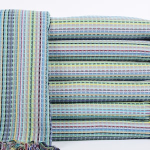 May include: A stack of colorful striped towels with fringed edges. The towels are folded and stacked on a white background.