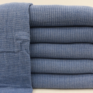 May include: A stack of five blue cotton towels with fringed edges. The towels are folded and stacked neatly.