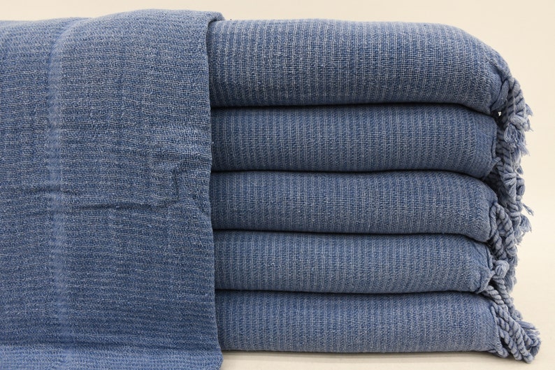 May include: A stack of five blue cotton towels with fringed edges. The towels are folded and stacked neatly.