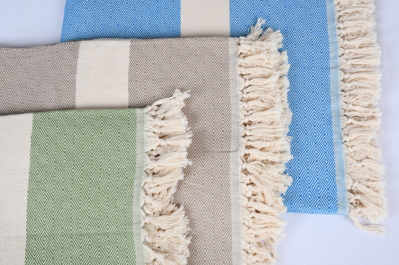 May include: Three striped towels with fringe. The towels are in shades of green, brown, and blue. Each towel has a diamond pattern.
