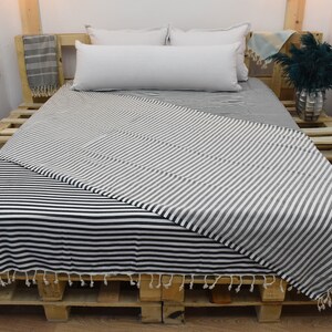 May include: A black and white striped throw blanket is draped over a wooden bed frame. The blanket has a fringe border and is made of a soft, comfortable fabric.