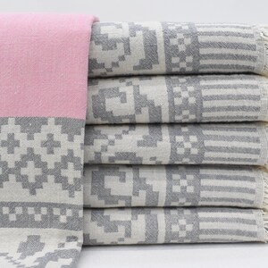 May include: A stack of five gray and white patterned towels with pink and gray patterned towel on top. The towels have a fringe edge.