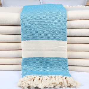 May include: A stack of white towels with a blue and white patterned towel folded on top. The blue and white towel has a fringe border.