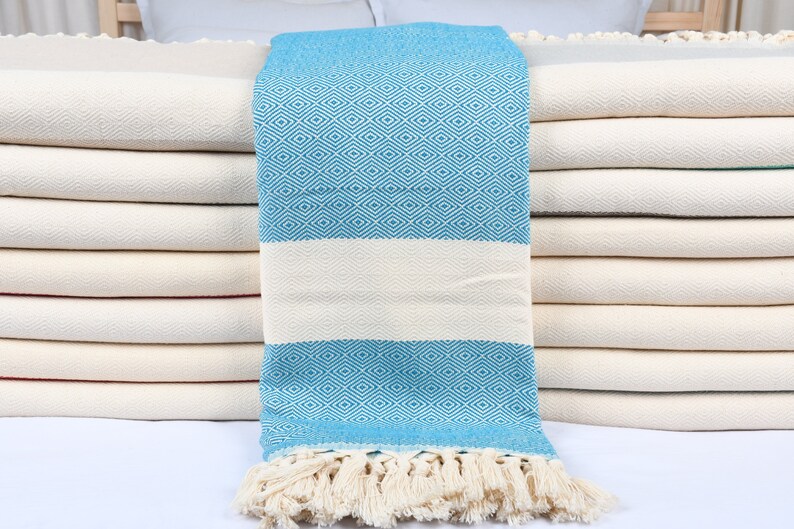 May include: A stack of white towels with a blue and white patterned towel folded on top. The blue and white towel has a fringe border.