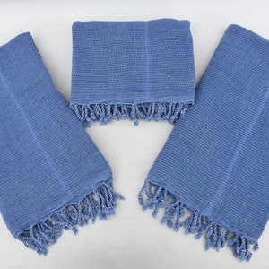 May include: Three blue cotton towels with fringe edges. The towels are folded and arranged on a white surface.