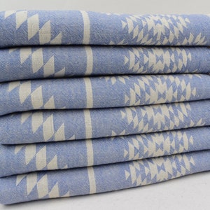 Peut inclure: Une pile de six serviettes de bain bleues et blanches &agrave; motifs avec des franges sur les bords. Les serviettes sont pli&eacute;es et empil&eacute;es sur une surface blanche.