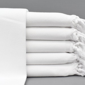 May include: A stack of white towels with fringed edges. The towels are folded and arranged neatly.
