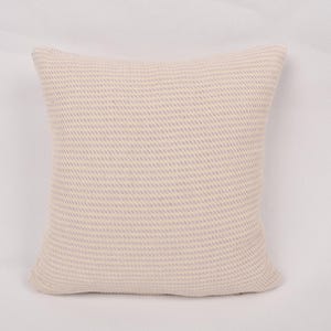 May include: A square decorative pillow with a woven texture. The pillow is a light beige color with a subtle pattern. The pillow is approximately 18 inches square, suitable for a sofa or bed.