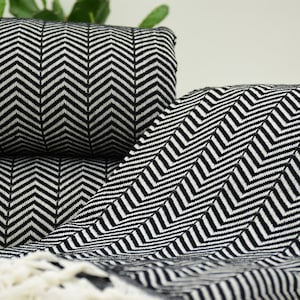 Pode incluir: Cobertor de chevron preto e branco com borda de franja. O cobertor está dobrado ao meio e as pontas estão enroladas.