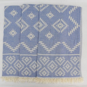 Peut inclure: Une serviette turque &agrave; motifs bleus et blancs avec une bordure en franges. La serviette pr&eacute;sente un motif g&eacute;om&eacute;trique avec des diamants et des triangles blancs sur un fond bleu clair.