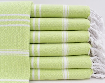 May include: A stack of light green Turkish towels with white stripes and white fringe. The towels are folded and stacked on a white surface.