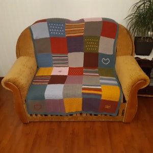 Könnte beinhalten: Eine mehrfarbige gestrickte Patchwork-Decke mit Herz- und Sternmuster, drapiert über einen braunen Sessel.