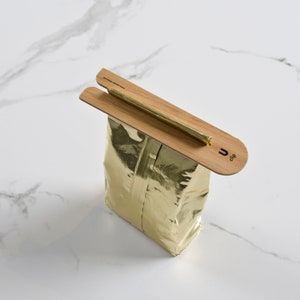 May include: A gold-colored bag with a bamboo clip that says "U clip" on it. The clip is used to seal the bag.
