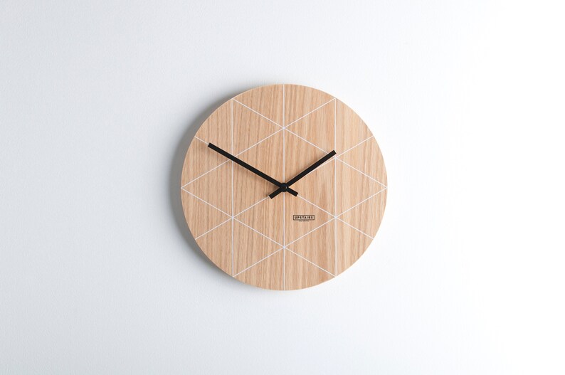 Puede incluir: Un reloj de madera redondo con un patr&oacute;n geom&eacute;trico blanco y agujas negras. La esfera del reloj tiene el texto "UPSTAIRS" impreso.