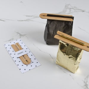 May include: Two sets of wooden bag clips, one set is on a white background with a pattern of the letter U, the other two clips are on a black and gold bag.