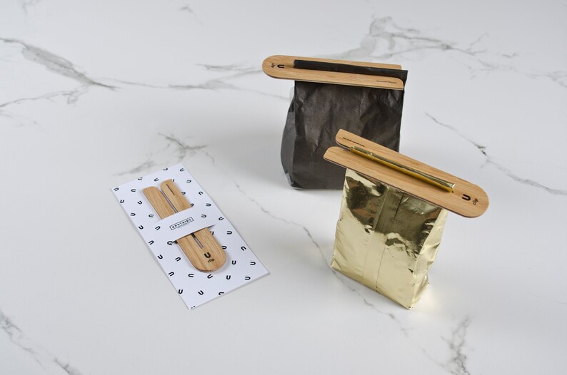 May include: Two sets of wooden bag clips, one set is on a white background with a pattern of the letter U, the other two clips are on a black and gold bag.