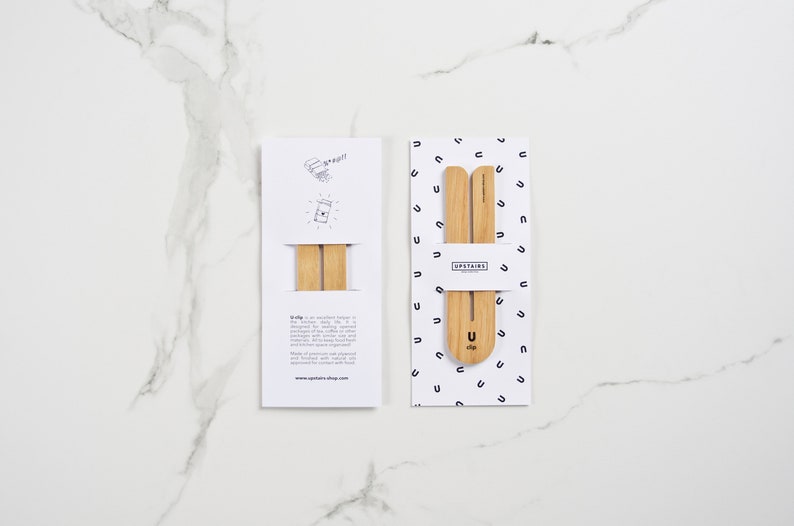 May include: Two packages of wooden U-clips, a product designed to help keep bags of coffee beans fresh. The packaging is white with black text and a simple illustration of the product. The text on the packaging reads "Upstairs" and "U-clip".