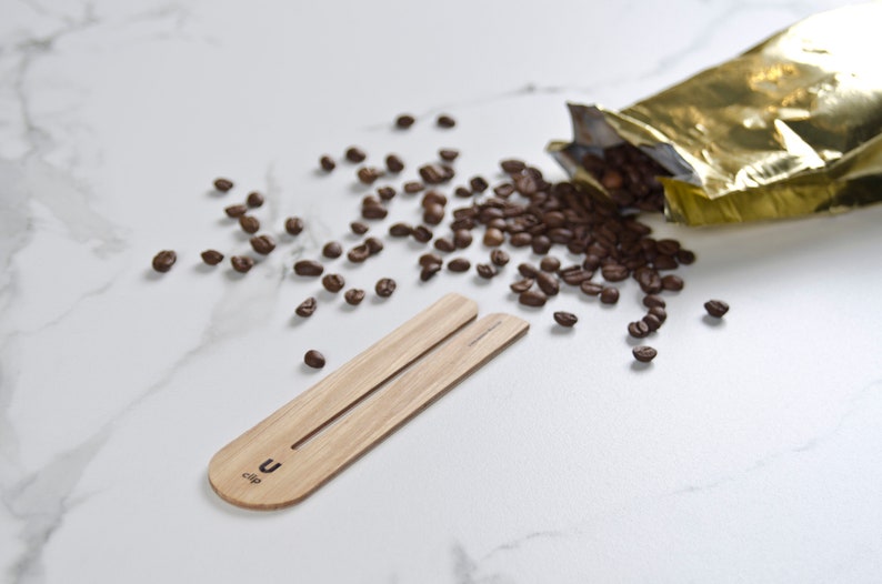 May include: A wooden coffee scoop with the text "U-clip" on it. The scoop is on a white marble surface with coffee beans scattered around it.