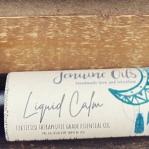 May include: A black roller bottle with a white label that says "Genuine Oils Handmade Love and Intention Liquid Calm Certified Therapeutic Grade Essential Oil". The label also features a blue and white dreamcatcher design.