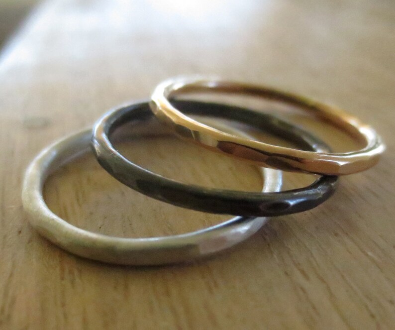May include: Three simple bands stacked together. The top band is gold, the middle band is black, and the bottom band is silver.