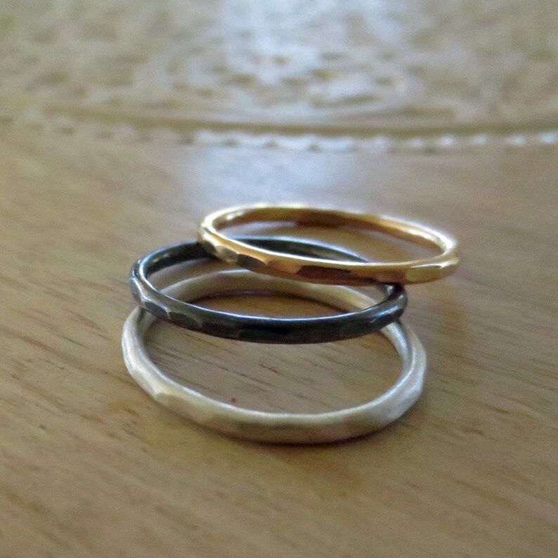 May include: Three simple hammered metal bands in gold, silver, and black. The bands are stacked on top of each other.