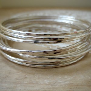 May include: A set of silver hammered bangle bracelets. The bracelets are stacked on top of each other, creating a layered look.
