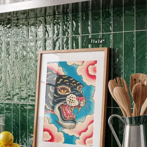 May include: A framed 11x14 inch art print featuring a stylized black panther head with yellow eyes and an open mouth, set against a blue background with pink clouds. The print is enclosed in a light-colored wooden frame with a white mat border.