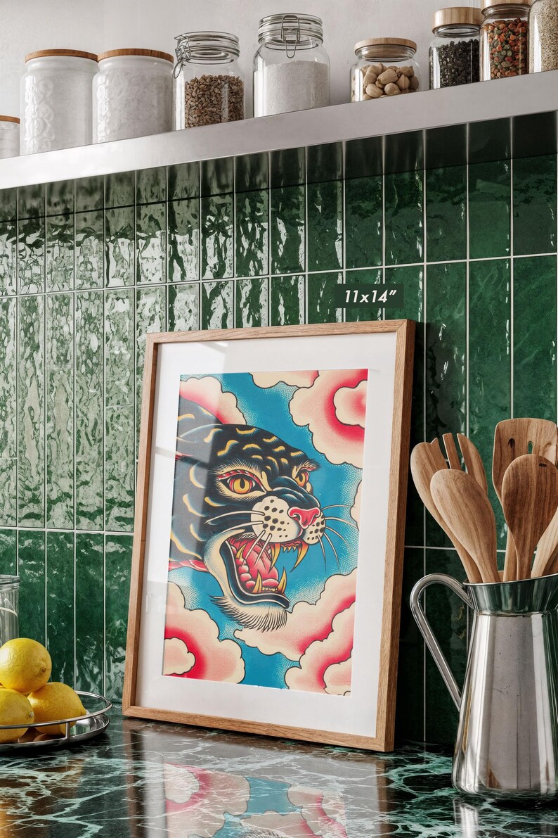 May include: A framed 11x14 inch art print featuring a stylized black panther head with yellow eyes and an open mouth, set against a blue background with pink clouds. The print is enclosed in a light-colored wooden frame with a white mat border.