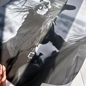 May include: A black and white photograph of a woman wearing a cowboy hat and a bandana, holding a gun. She is riding a horse, and the image is cropped at the top and bottom.