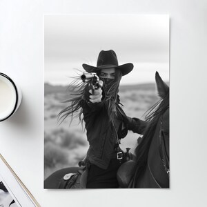 May include: A woman wearing a black cowboy hat and a black bandana over her face is riding a horse. She is holding a gun in her right hand and pointing it forward. The photo is in black and white.