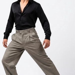 May include: A black long-sleeved button-down shirt with a collar and a pair of pleated taupe trousers featuring a subtle vertical pinstripe pattern, a high waist, and cuffed hems, paired with two-toned black and brown leather dress shoes.