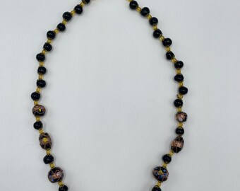 May include: A black and gold beaded necklace with colorful patterned beads. The necklace is made of glass beads and has a simple clasp.