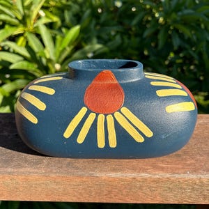May include: A dark blue ceramic vase with a rounded shape. The vase is decorated with yellow and orange painted floral designs. The vase is sitting on a wooden surface.
