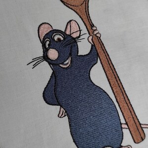 Puede incluir: Imagen bordada de una rata de dibujos animados sosteniendo una cuchara de madera. La rata es azul y tiene la nariz y las orejas rosas. La cuchara es marr&oacute;n.