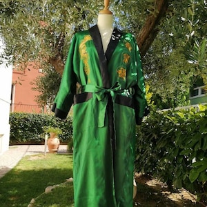 Könnte beinhalten: Eine grüne Seidenrobe mit goldener Stickerei eines Drachen und anderer chinesischer Symbole. Die Robe hat einen schwarzen Besatz und eine schwarze Schärpe.