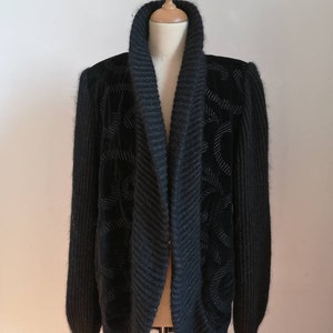 May include: A black knit cardigan with a wide, shawl collar and a textured pattern. The cardigan is made of a soft, fuzzy material.