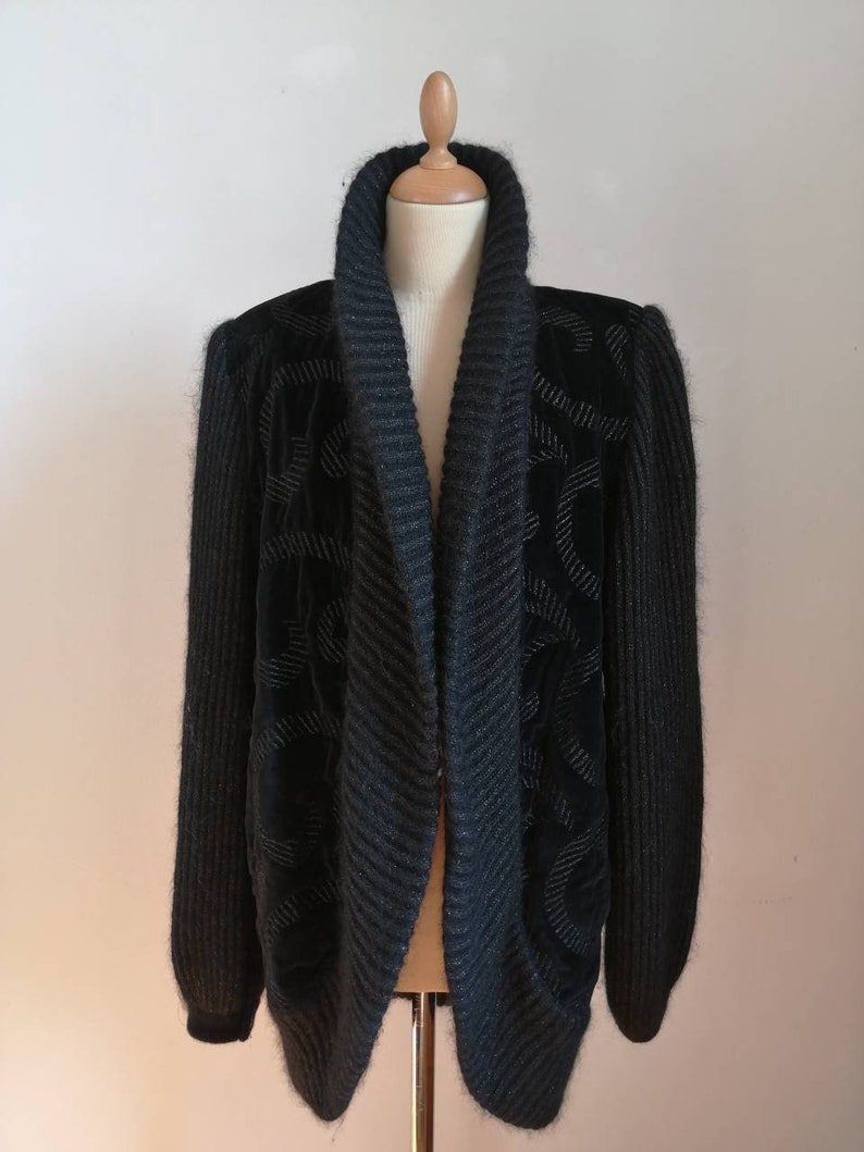 May include: A black knit cardigan with a wide, shawl collar and a textured pattern. The cardigan is made of a soft, fuzzy material.