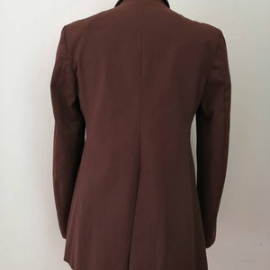 Pu&ograve; includere: Un blazer marrone con una silhouette lunga e aderente. Il blazer ha una chiusura a un solo bottone e maniche lunghe.