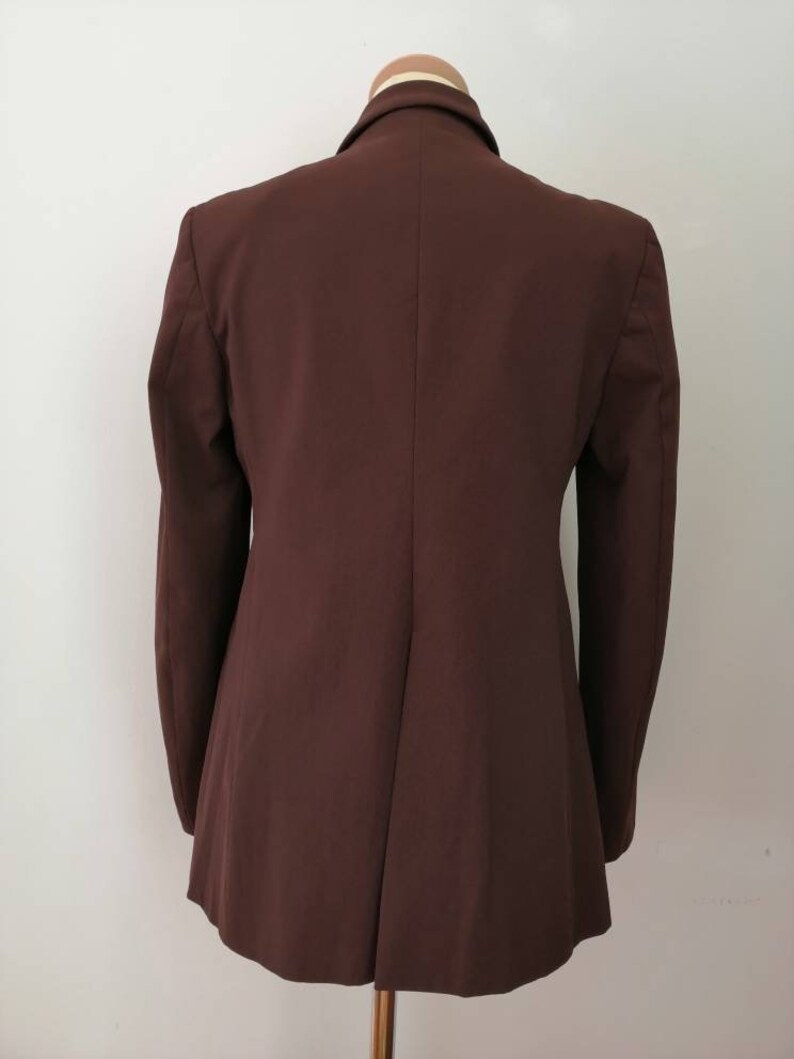 Pu&ograve; includere: Un blazer marrone con una silhouette lunga e aderente. Il blazer ha una chiusura a un solo bottone e maniche lunghe.