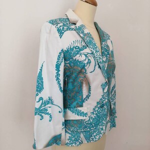 May include: A white blazer with a teal floral pattern. The blazer has a notched collar, long sleeves, and a single button closure.