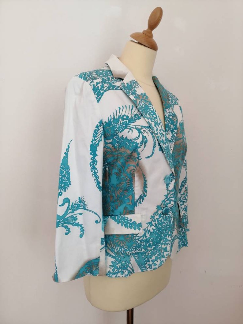 May include: A white blazer with a teal floral pattern. The blazer has a notched collar, long sleeves, and a single button closure.