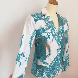 May include: A white blazer with a teal floral pattern. The blazer has a notched collar, long sleeves, and a single button closure.