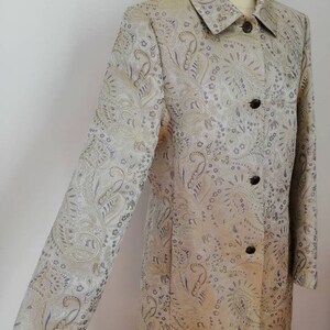 May include: A long-sleeved jacket with a paisley pattern in shades of gold, silver, and purple. The jacket has a collared neckline and a button closure.