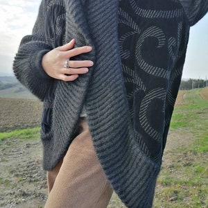 May include: A gray and black cardigan with a black velvet panel featuring a swirl design. The cardigan is open in the front and has a ribbed texture.