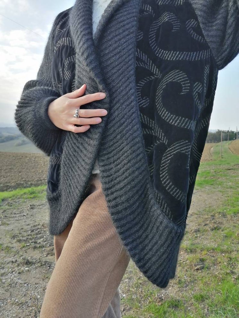 May include: A gray and black cardigan with a black velvet panel featuring a swirl design. The cardigan is open in the front and has a ribbed texture.