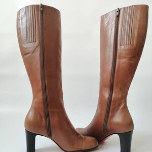May include: A pair of brown leather knee-high boots with a block heel. The boots have a zipper on the inside of each boot.