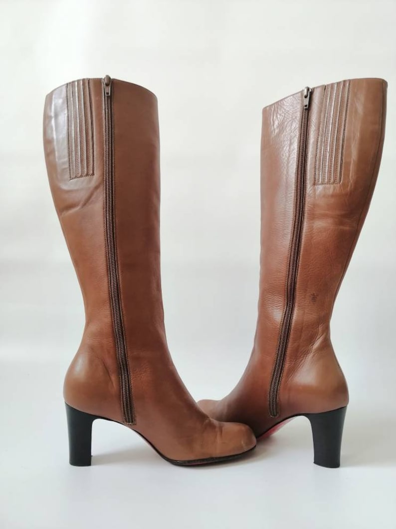 May include: A pair of brown leather knee-high boots with a block heel. The boots have a zipper on the inside of each boot.