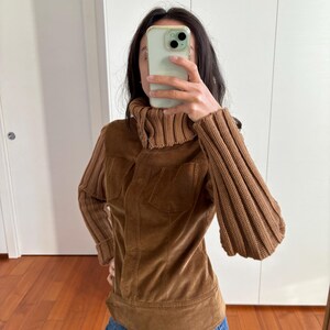 May include: A brown corduroy jacket with a turtleneck collar and ribbed knit sleeves. The jacket has a zipper closure and a fitted silhouette.